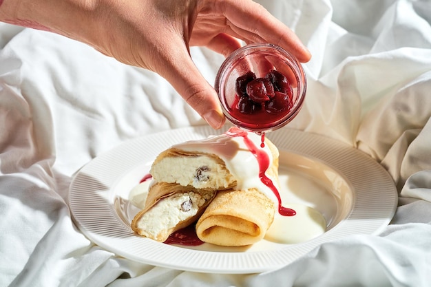 Crepes con requesón y mermelada en un plato sobre una sábana blanca Se vierte mermelada de luz dura sobre los panqueques