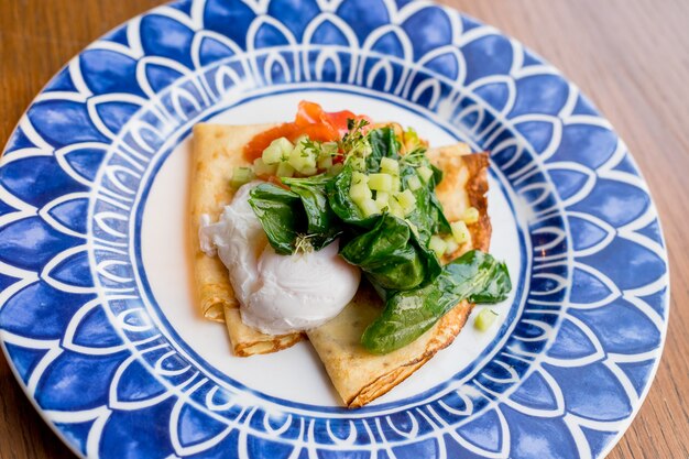 Crepes salados con salmón y huevo escalfado. Sabroso desayuno con panqueques, salmón ahumado, huevo empacado con espinacas, lechuga, cebolla, salsa holandesa. Desayuno fresco y saludable.