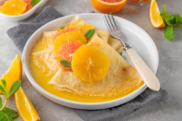 crepes suzette com calda de laranja e fatias de frutas em um prato em uma vista superior de fundo cinza de concreto