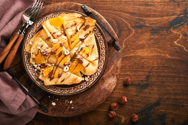 Crepes suzette com laranjas e chocolate Crepes finos com chocolate espalhar avelãs e fatias de laranja frutas no prato para o café da manhã no antigo fundo de mesa rústica de madeira escura Copiar espaço Vista superior