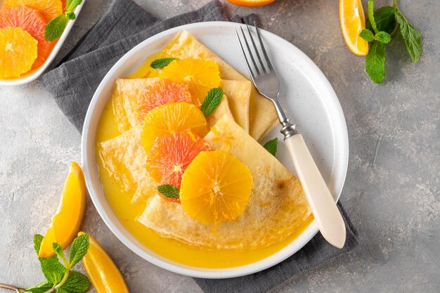 crepes suzette con jarabe de naranja y rodajas de frutas en un plato sobre un fondo de hormigón gris