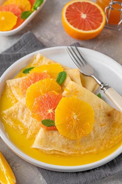 crepes suzette con jarabe de naranja y rodajas de frutas en un plato sobre una vista superior de fondo de hormigón gris