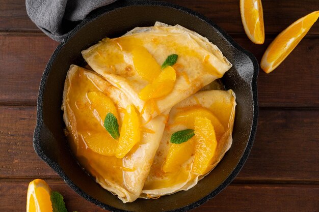 Crêpes Suzette mit Orangensirup und Obstscheiben auf einer Bratpfanne auf dunklem Holzhintergrund