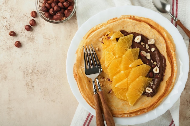 Crepes suzette con naranjas Crepes finas con chocolate, avellanas y rodajas de naranja, fruta en un plato blanco para el desayuno en el antiguo fondo de mesa rústico de hormigón Espacio de copia Vista superior