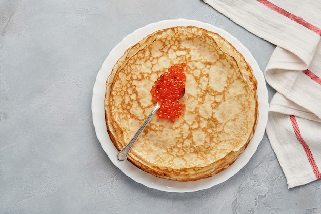 Crepes, tortitas finas, tortitas rusas con caviar rojo sobre placa gris. Fondo de mármol. Copie el espacio. Vista superior.