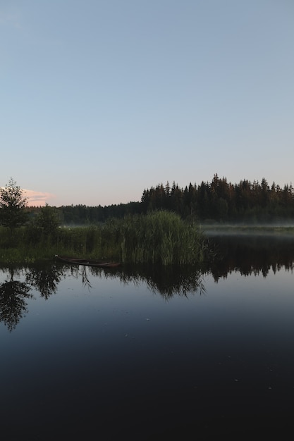 Crepúsculo vespertino de verano vista sobre la pintoresca superficie llana del lago con reflejos del cielo y los árboles