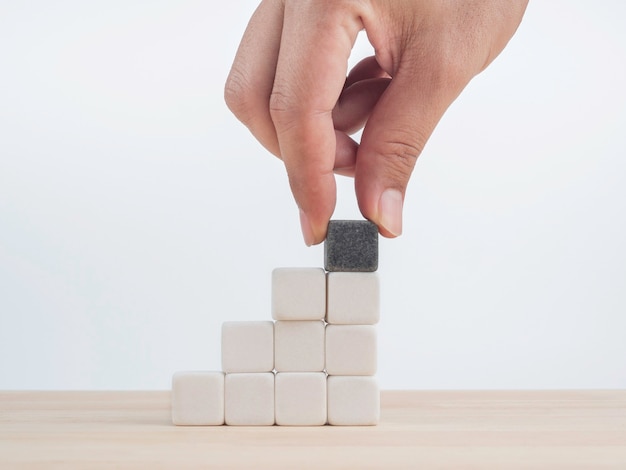 Foto crescimento do negócio, conceito de processo de construção de benefícios. mão colocou o último bloco de cubo de dados preto uma diferença em cima de blocos de dados brancos de empilhamento como escada de degrau na mesa de madeira no fundo branco.