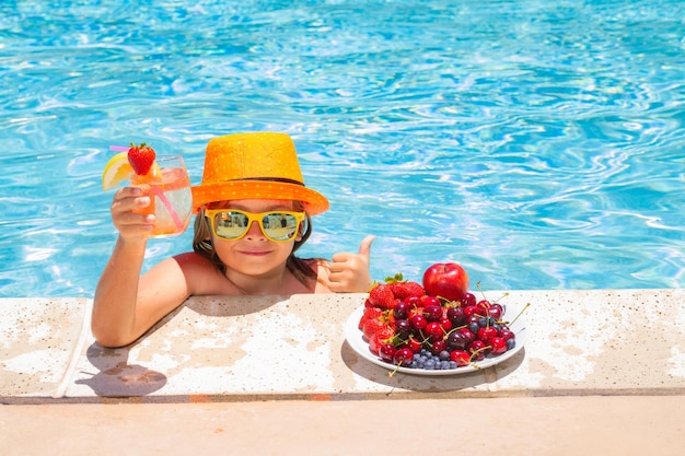 Criança à beira da piscina comendo frutas e bebendo coquetel de limonada Conceito de férias para crianças de verão