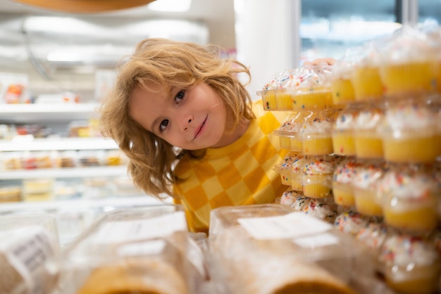 Criança a escolher bolos, cupcakes, muffins no supermercado, criança a fazer compras.