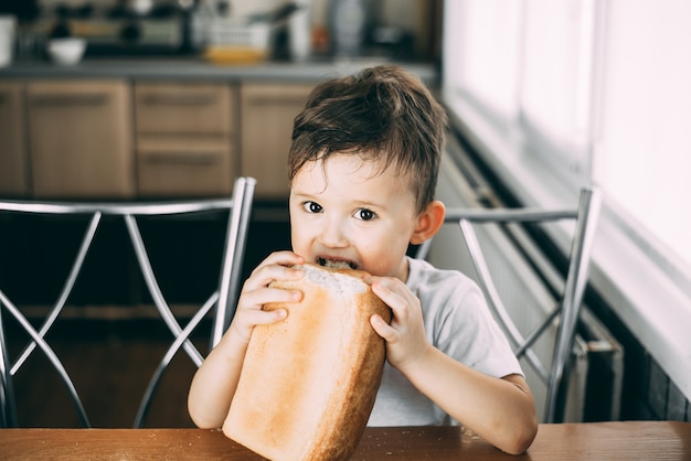 Criança à mesa durante o dia come avidamente um pão inteiro em forma de tijolo