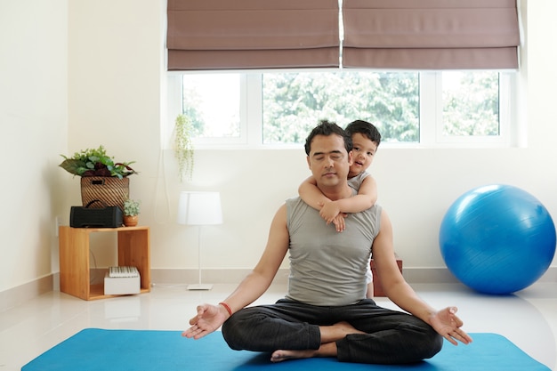 Criança abraçando o pai meditando em casa em posição de lótus tentando encontrar uma peça interior