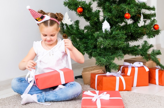 Criança abrindo presentes de natal. criança debaixo da árvore de natal com caixas de presente.