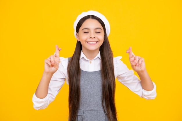 Criança adolescente alegre feliz desejando boa sorte cruza os dedos tem fé para melhor isolado sobre fundo amarelo