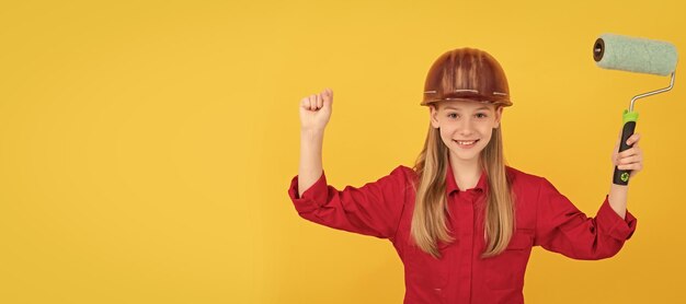 Criança adolescente feliz em capacete de construtor com rolo de pintura na parede amarela Construtor de criança em design de cartaz horizontal de capacete Espaço de cópia de cabeçalho de banner