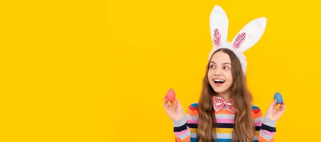 Criança adolescente feliz em orelhas de coelho e gravata borboleta seguram ovos de páscoa em fundo amarelo Pôster horizontal de criança de Páscoa Cabeçalho de banner da Web do espaço de cópia de criança de coelho