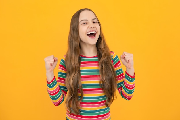 Criança adolescente muito feliz com sucesso fazer gesto de vencedor cerrar o punho dizer sim isolado no estúdio de fundo amarelo Rosto animado emoções alegres da menina adolescente