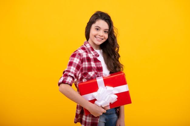 Criança adolescente na camisa segurando a caixa de presente em fundo amarelo isolado Presente para aniversário de crianças Feliz adolescente emoções positivas e sorridentes de adolescente