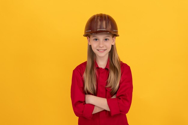 Criança adolescente positiva no capacete do construtor em fundo amarelo