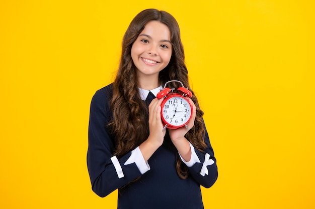 Criança adolescente segura relógio isolado no fundo amarelo do estúdio Criança adolescente com despertador mostrando o tempo