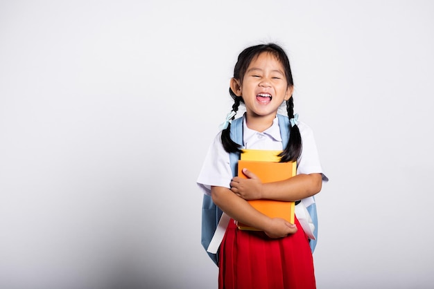 Criança adorável asiática sorrindo feliz vestida estudante tailandesa uniforme saia vermelha ficar segurando ou abraçando livro