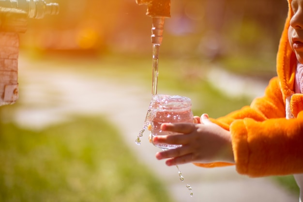 criança adorável brincando com água e torneira ao sol