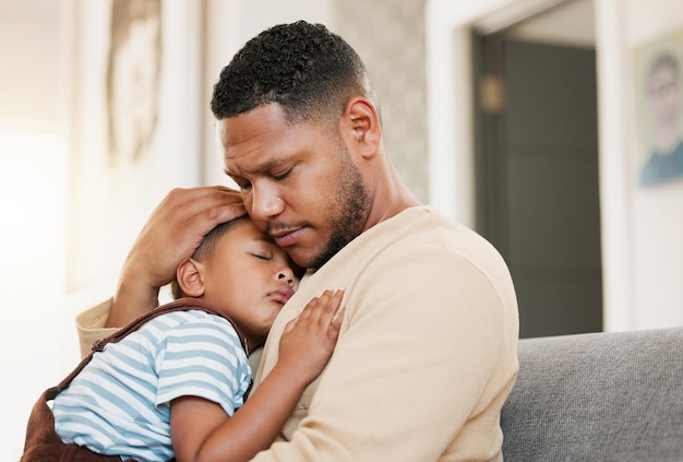 Foto criança adormecida e cansada com pai carinhoso segurando seu filho sonolento em um sofá de sala de estar pai preocupado abraçando seu filho descansando em um sofá de família da sala de estar dentro de casa sentindo estresse e preocupação