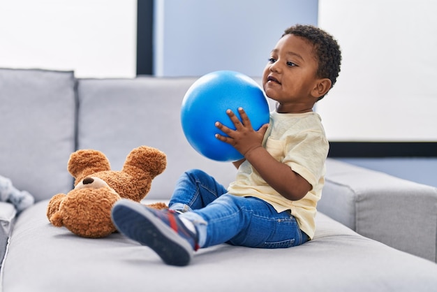 Criança afro-americana brincando com bola sentada no sofá em casa