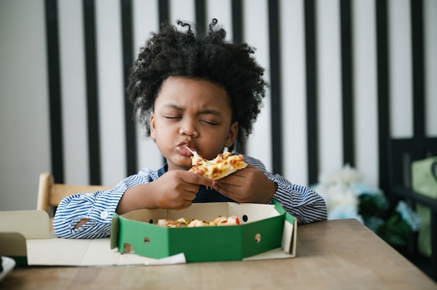 Criança afro-americana feliz comendo pizza na mesa