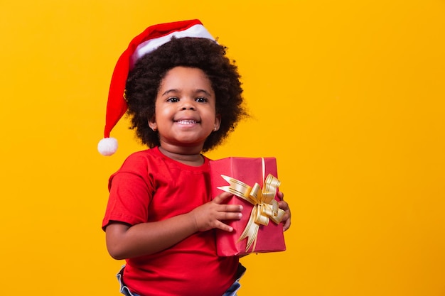 Foto criança afro sorridente com chapéu de papai noel vermelho segurando o presente de natal na mão. conceito de natal.