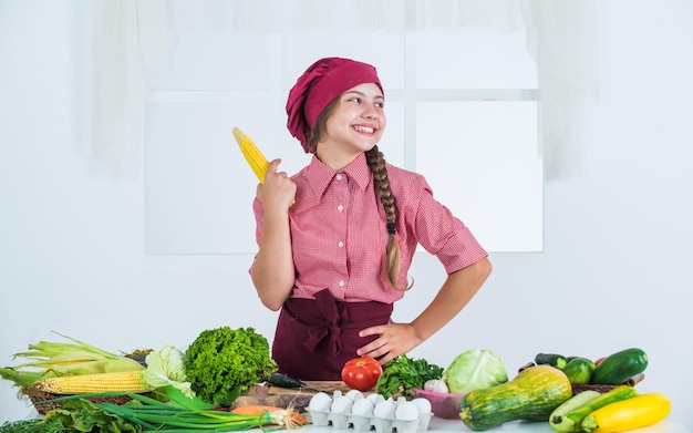 Criança alegre com milho e muitos vegetais úteis vegetarianos