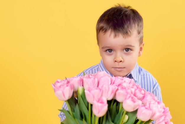 Criança alegre com um buquê de flores de tulipa rosa Menino sorridente em um fundo amarelo