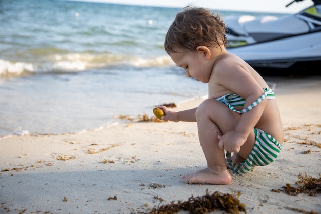 Criança alegre e feliz brincando com uma planta sentada à beira-mar