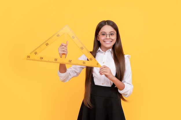 Criança alegre em uniforme escolar e óculos segura triângulo matemático para medição de medição