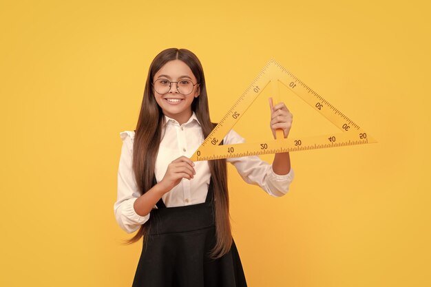 Criança alegre em uniforme escolar e óculos segura triângulo matemático para medição de medição