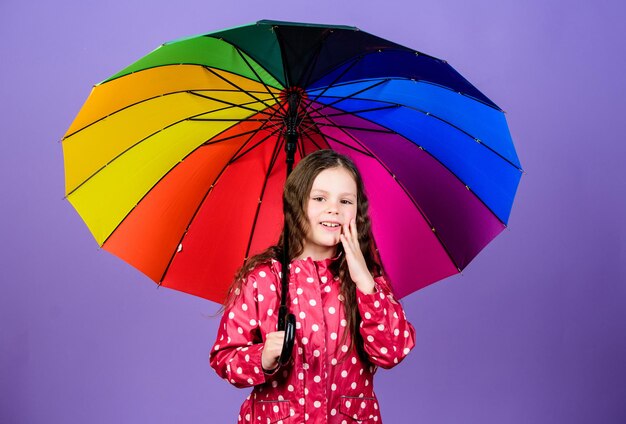 Criança alegre hipster de bom humor. Menina pequena na capa de chuva. moda outono. proteção contra chuva. Arco Iris. menina feliz com guarda-chuva colorido. Manhã tranquila.