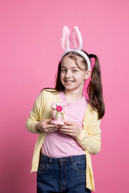 Criança alegre posando com um brinquedo de coelho rosa na câmera