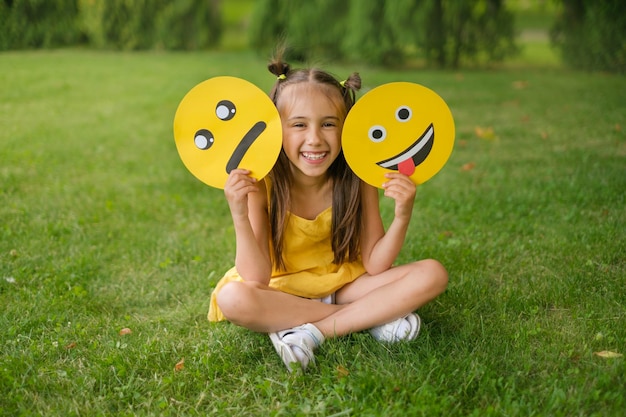 Criança alegre rindo tem dois emoticons nas mãos