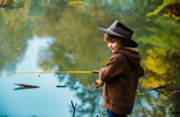 Foto criança aprendendo a pescar segurando uma vara em um lago criança com vara de pesca pequeno pescador com um chapéu