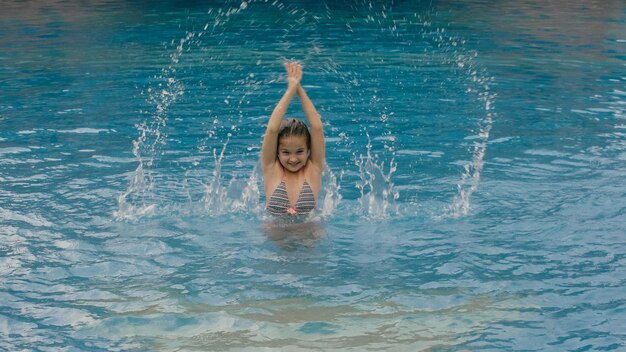 Criança aproveita as férias de verão em uma piscina pulando água de respingos giratórios