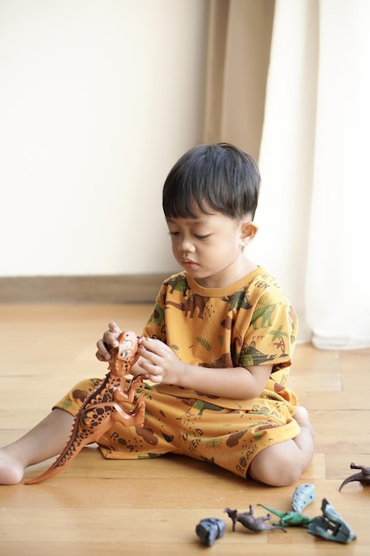 Criança asiática bonita brincando alegremente com um brinquedo de dinossauro de plástico perto da janela em um hotel