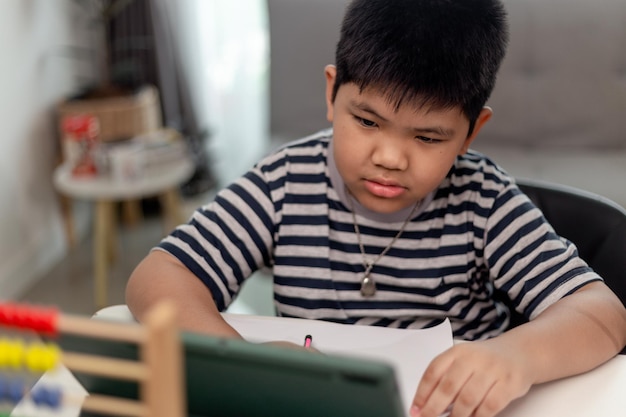 Criança asiática bonita estudando aula on-line com videochamada do tablet em casa Conceito de distanciamento social