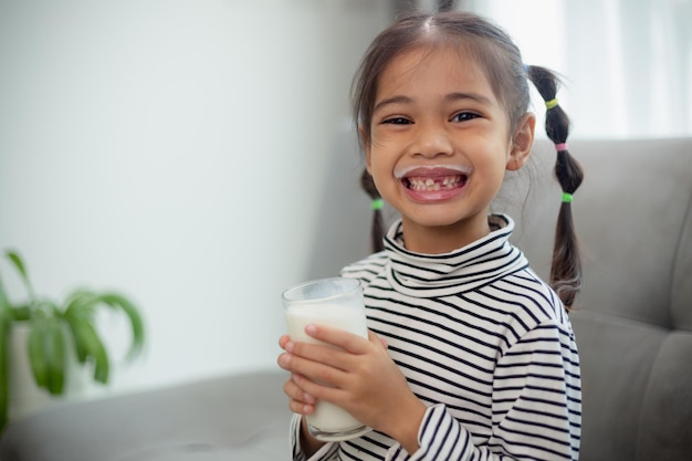 Criança asiática bonita segurando um copo de leite na casa se sentir feliz e gostar de beber leite