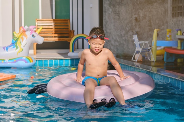 Criança asiática em óculos de natação e calção de banho relaxando em um anel inflável na villa da piscina