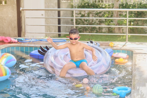 Criança asiática em óculos de natação e calção de banho relaxando em um anel inflável na villa da piscina