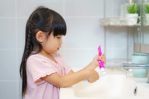 Criança asiática linda garota ou criança Esprema a pasta de dentes na escova de dentes