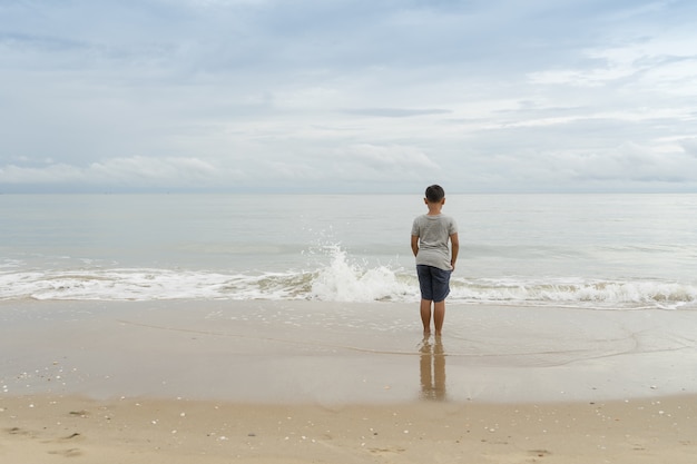 Criança asiática que está e que olha o mar no tempo do dia. conceito de lazer e pessoas