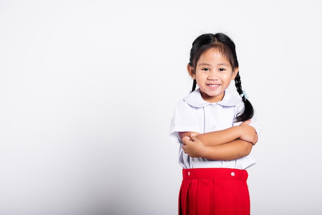 Criança asiática sorri feliz vestindo uniforme tailandês de saia vermelha de estudante com braços cruzados