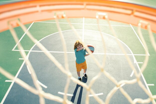 Criança atirando bola de basquete e jogando basquete vista inferior grande angular