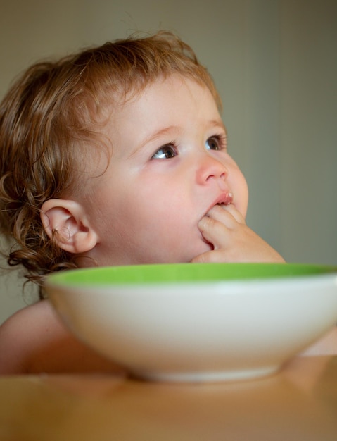Criança bebê comer sopa na cozinha com pratos e colher