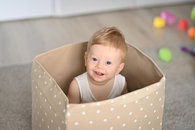 Criança bebê feliz sentado em uma caixa vazia em casa.